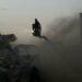 A person on a crane surveys the ruins of a bombed building, surrounded by smoke.